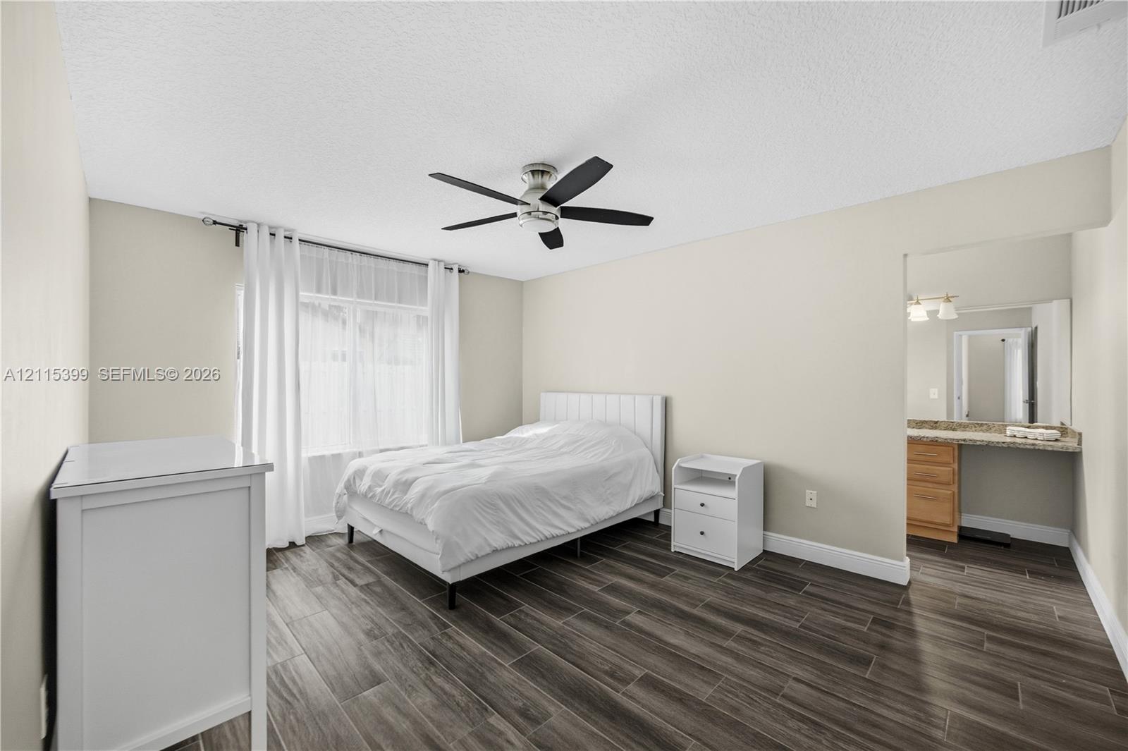 Wood-finish flooring, neutral wall color, ceiling fan with light fixture, and an integrated vanity area with stone-surface countertop