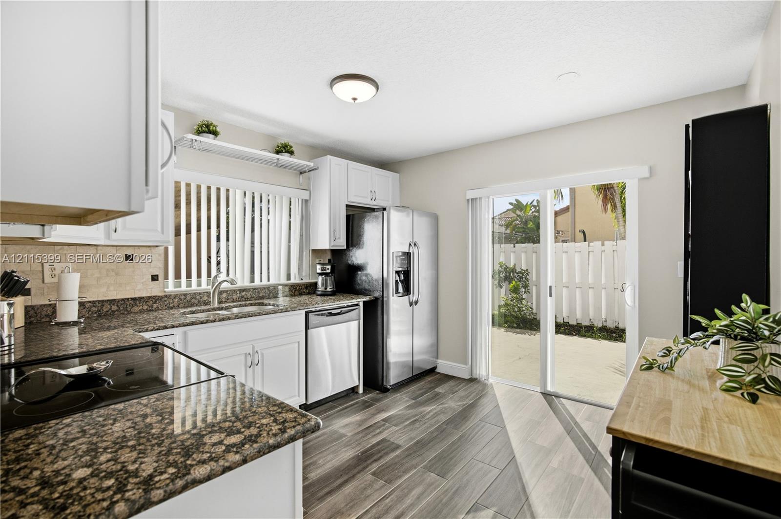 Kitchen featuring white cabinetry, stone-finish countertops, stainless steel appliances, wood-finish flooring, and a sliding glass door providing external access