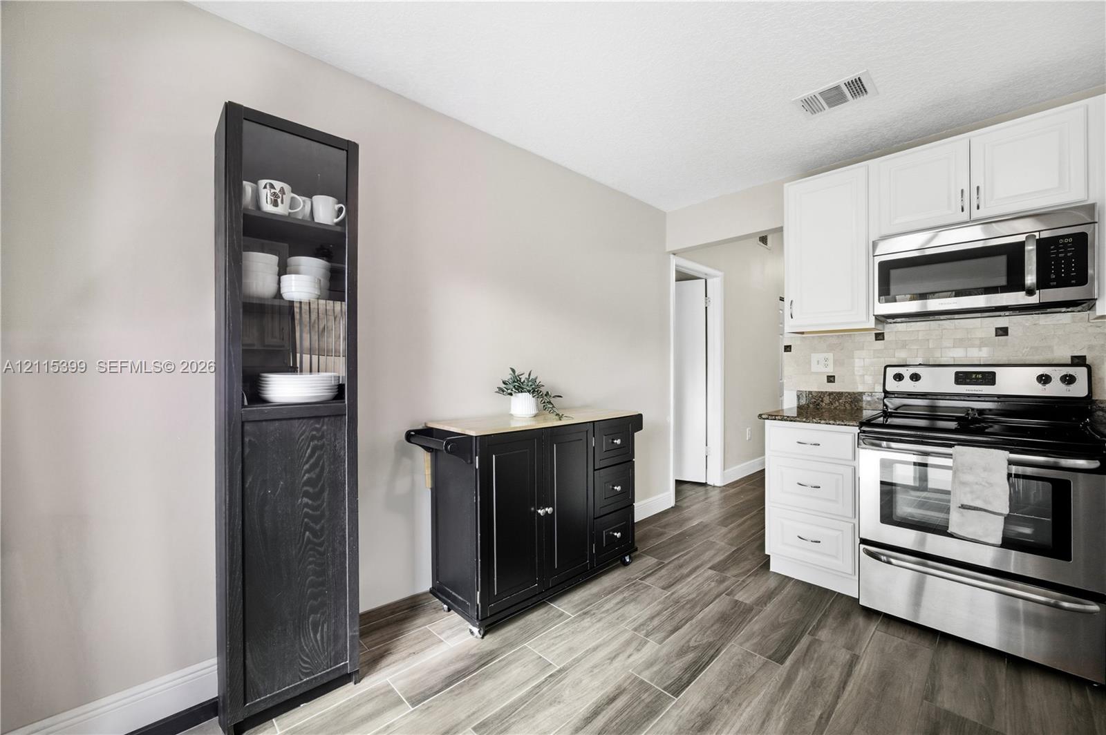 Kitchen featuring white cabinetry, stainless steel appliances, integrated over-the-range microwave, stone-finish countertops, and wood-finish flooring