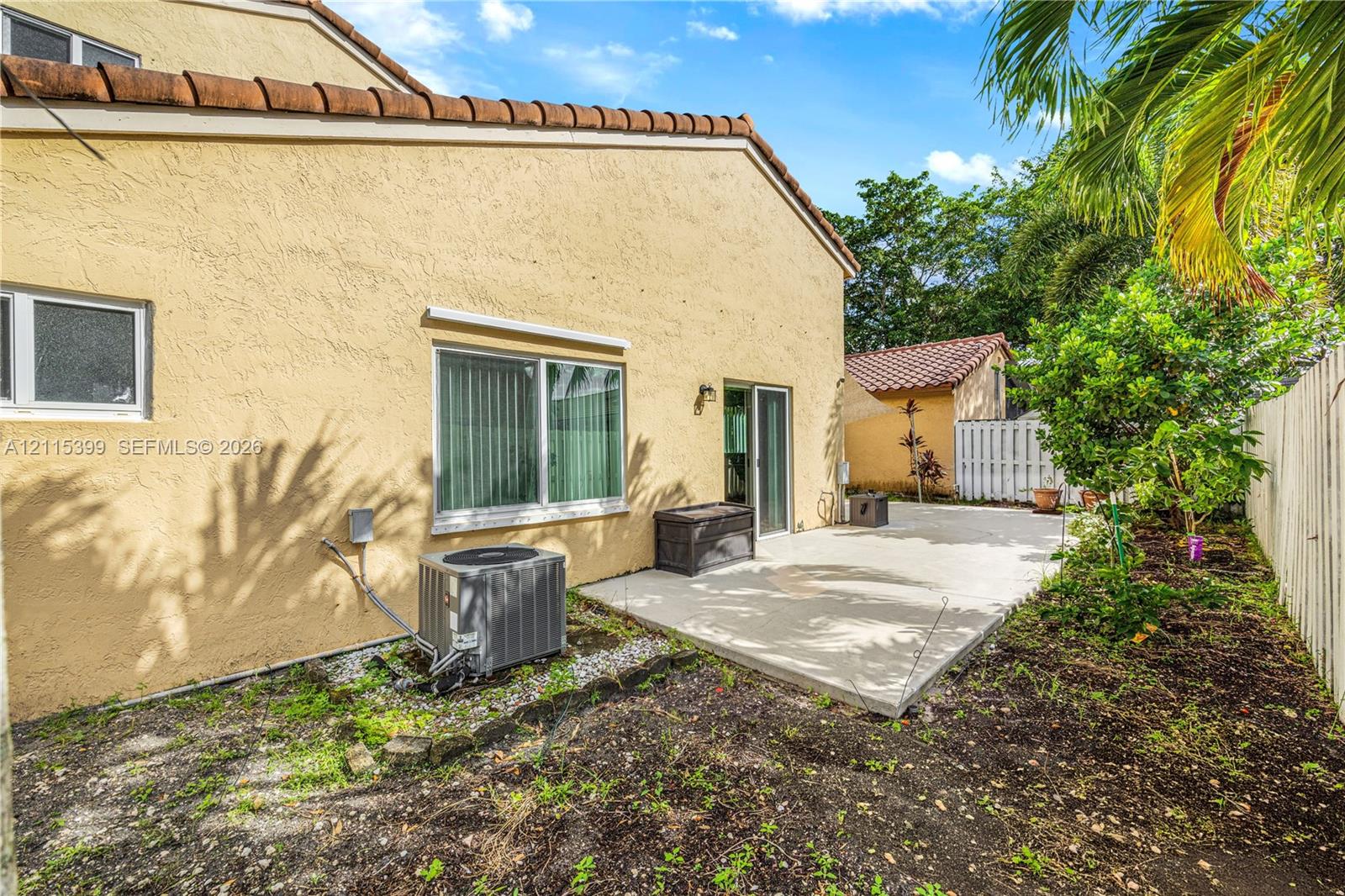 Stucco exterior featuring a concrete patio, sliding glass door, tiled roof, and perimeter fencing