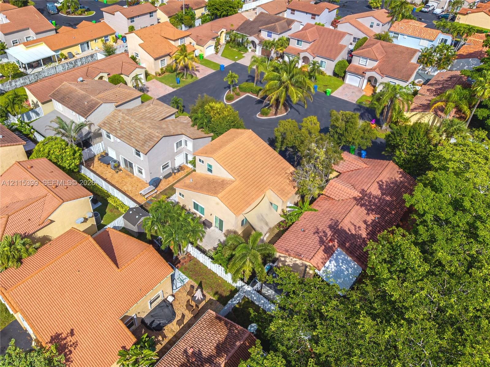 Aerial perspective of a multi-level residence featuring a clay tile roof, stucco exterior, fenced perimeter, and mature landscaping