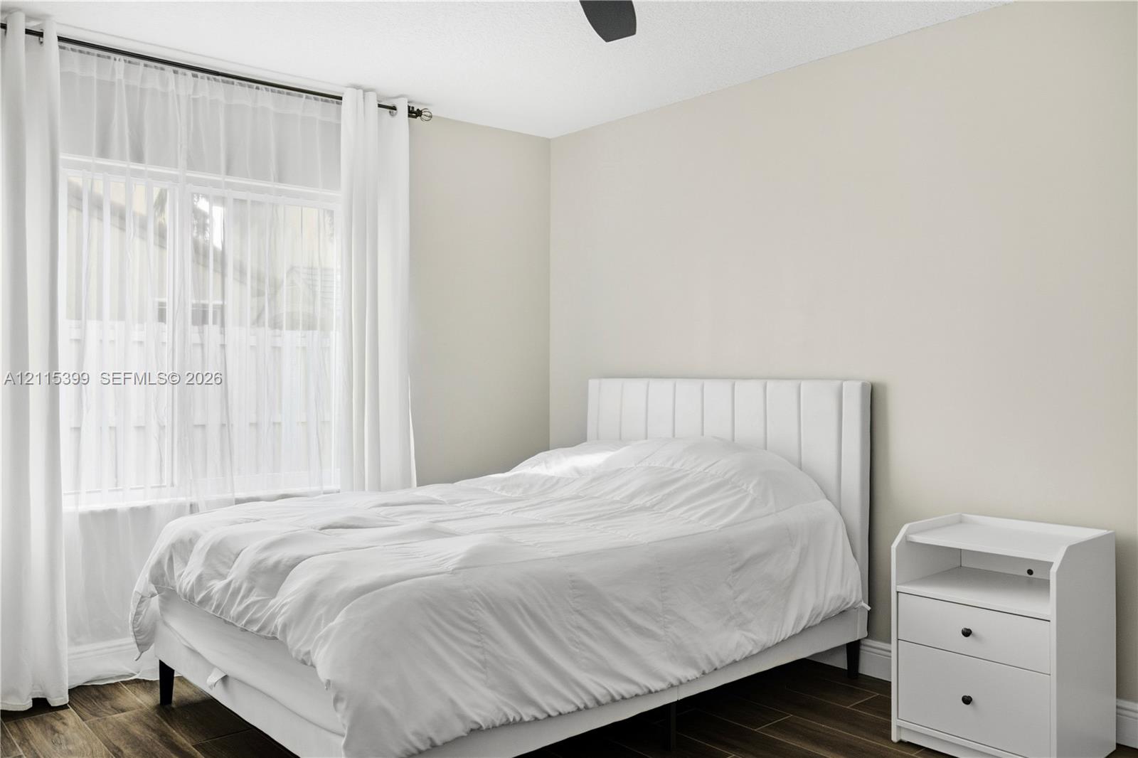 Neutral-toned interior space featuring wood-finish flooring, a dual-pane window with a curtain rod, and a ceiling fan