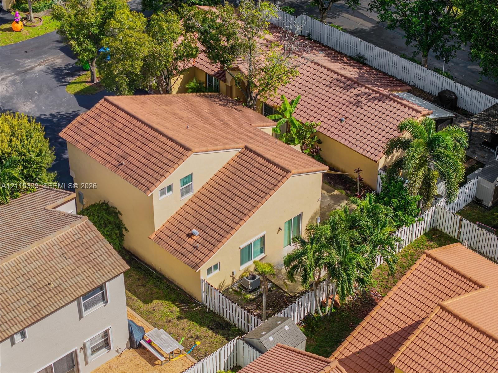 Multi-level residence featuring a clay tile roof, stucco exterior, fenced backyard, and mature palm trees