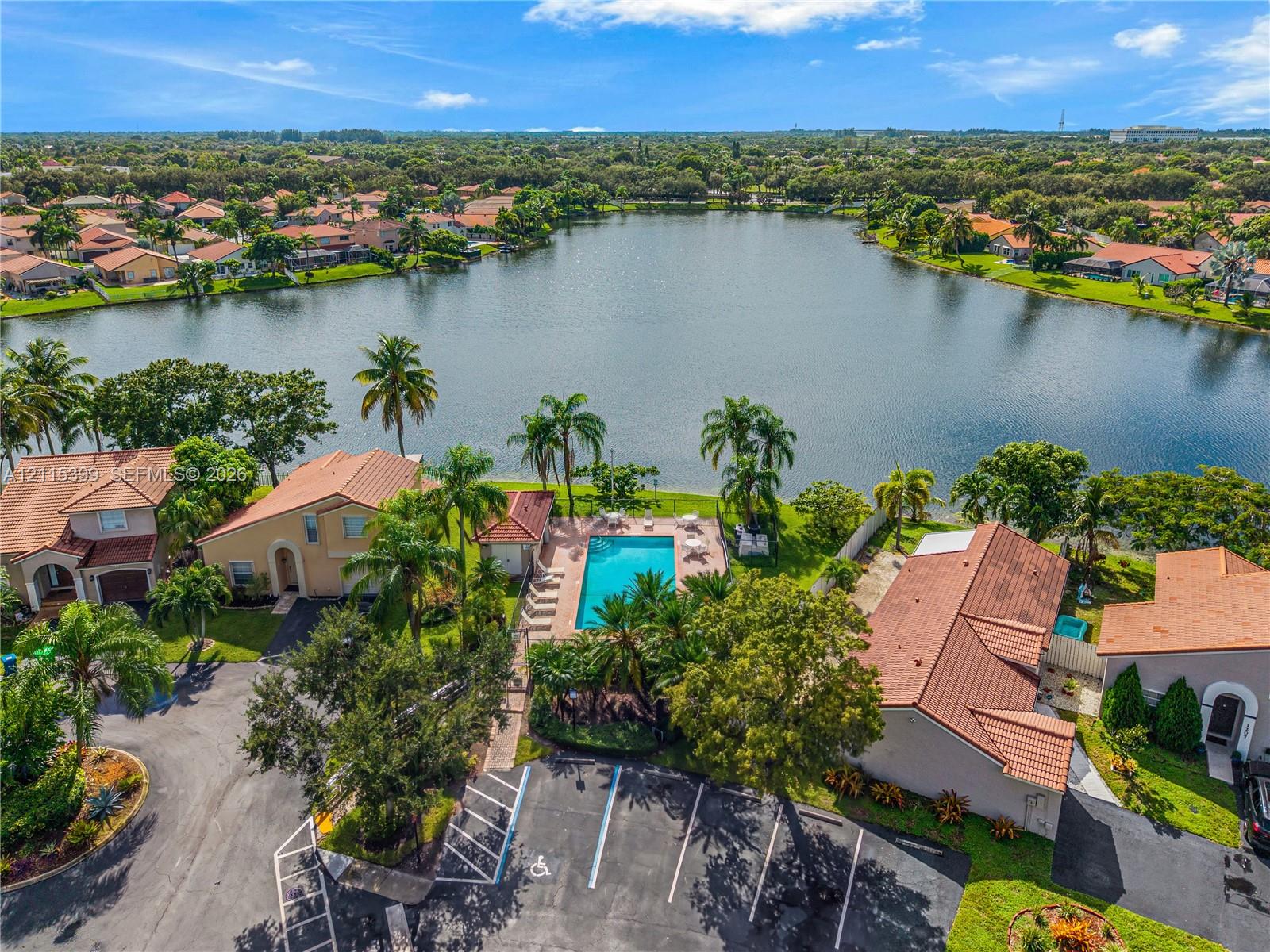 Aerial perspective featuring a communal swimming pool, paved parking area, tile-roof residential structures, and waterfront exposure