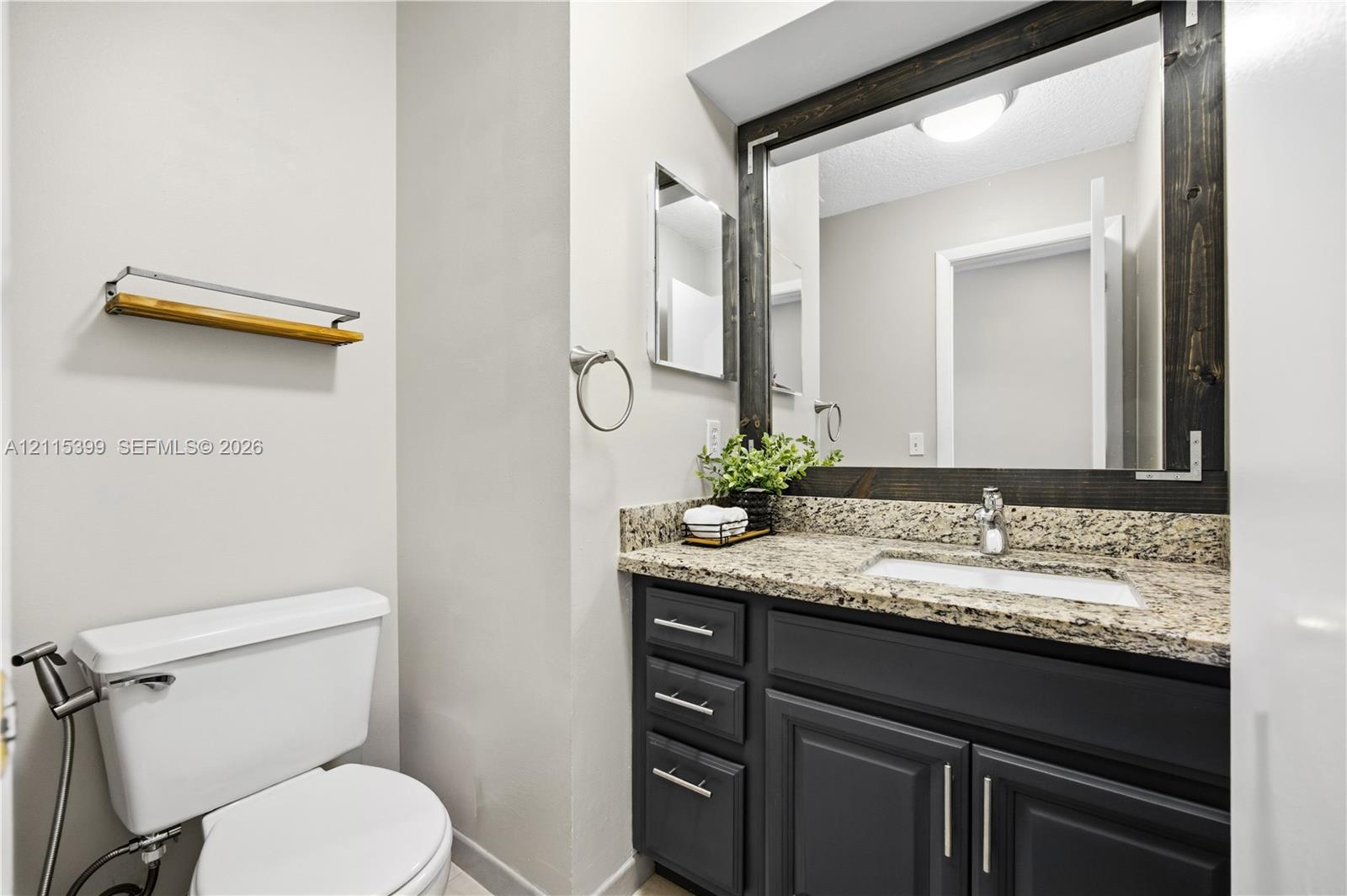 Bathroom featuring a stone-composite countertop, dark-toned cabinetry with brushed-metal pulls, an integrated rectangular sink, a decorative wood-framed mirror, and a wall-mounted wooden towel rack
