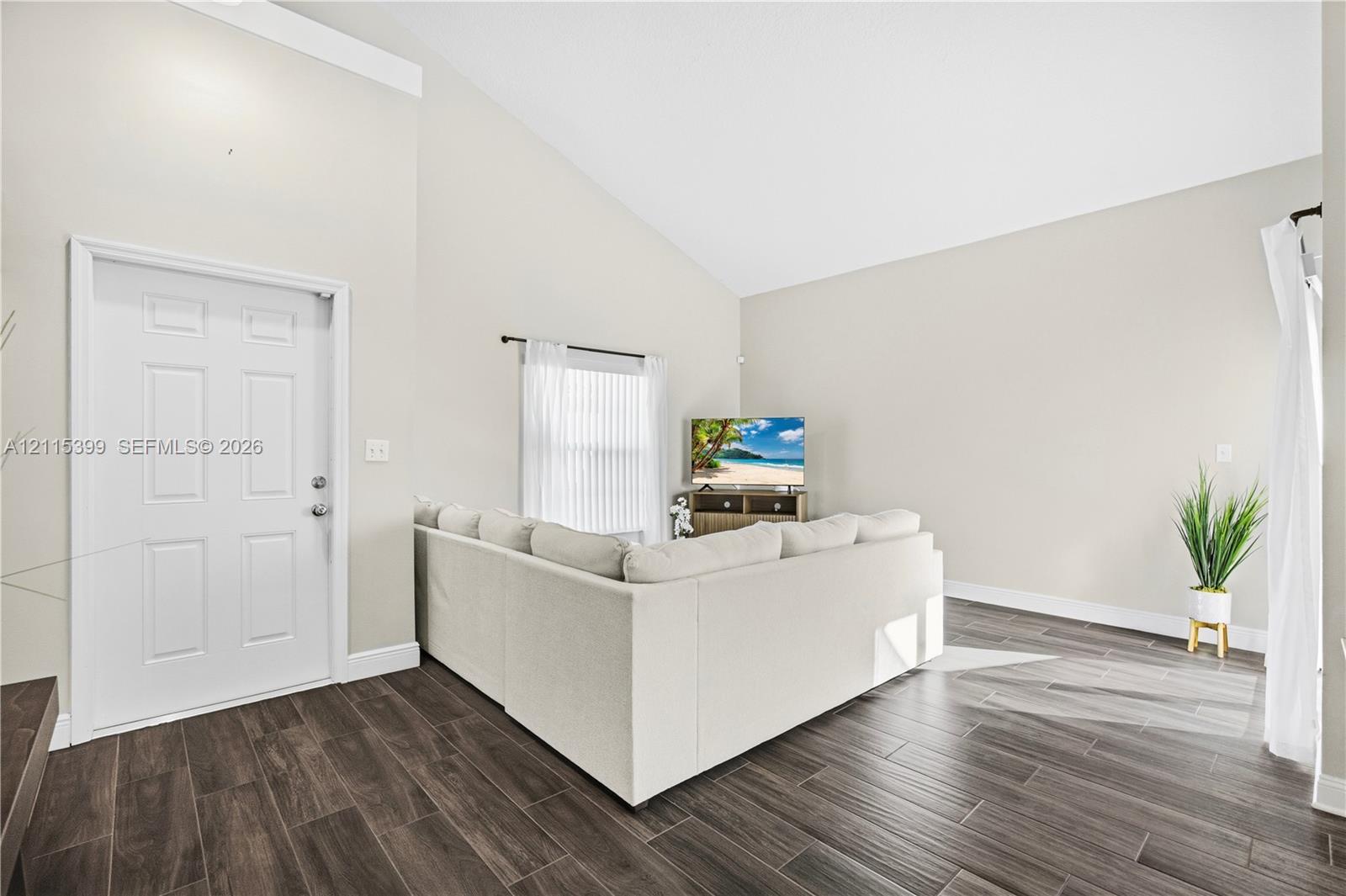 Vaulted ceilings and wood-finish flooring with a multi-panel entry door and window treatments
