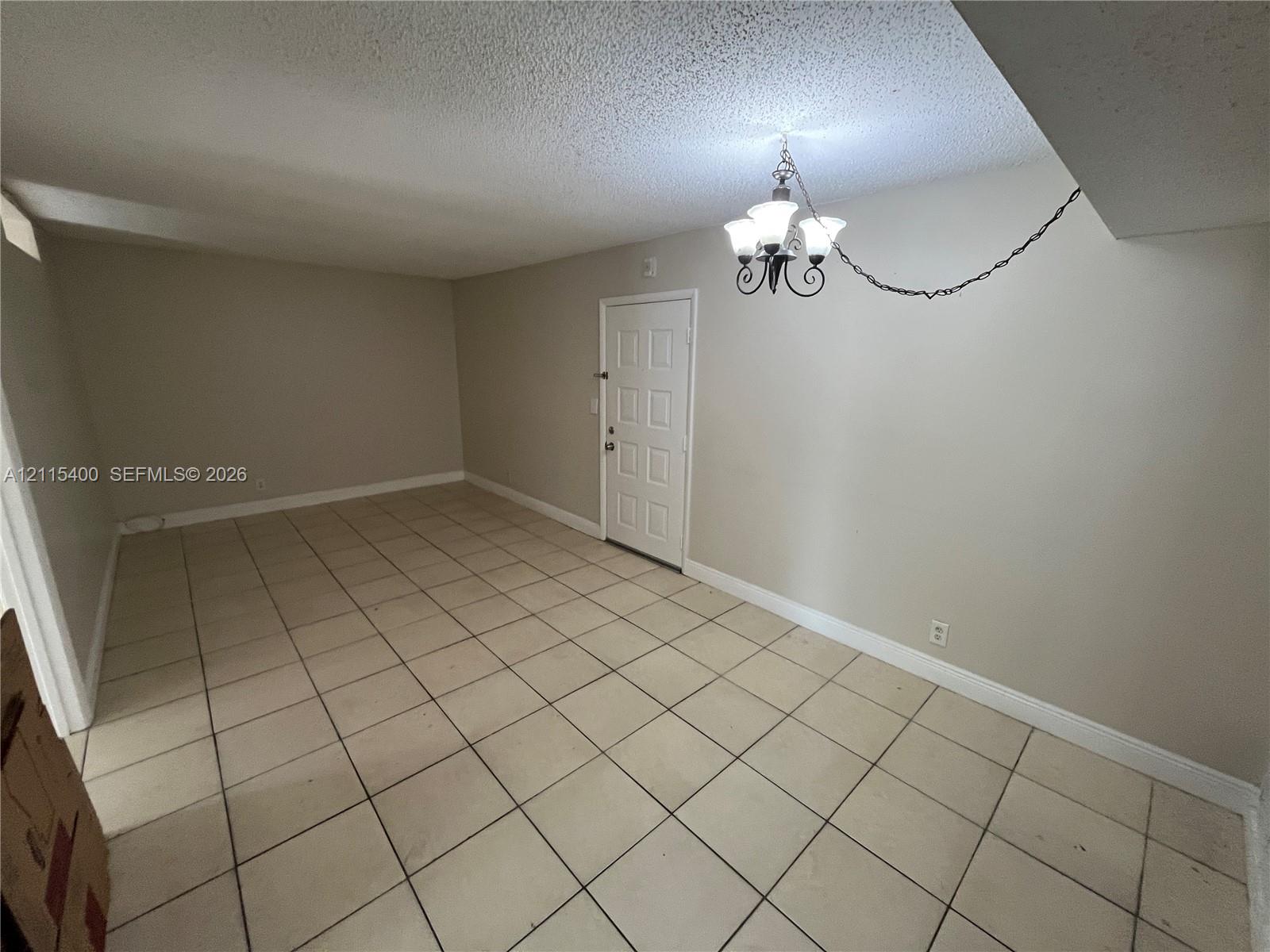 Interior space featuring neutral wall paint, ceramic tile flooring, a multi-panel door, and a suspended multi-light chandelier