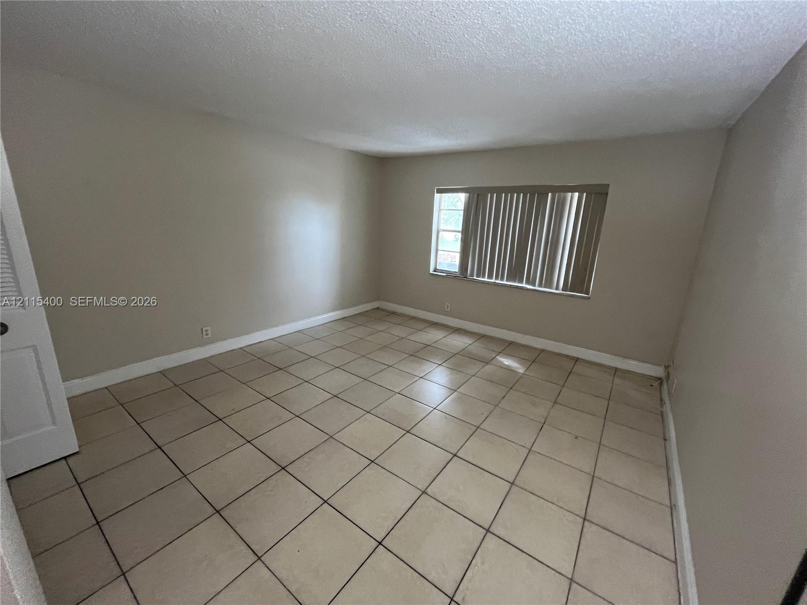 Neutral interior room featuring tile flooring, smooth-finish walls, and a window with vertical blinds