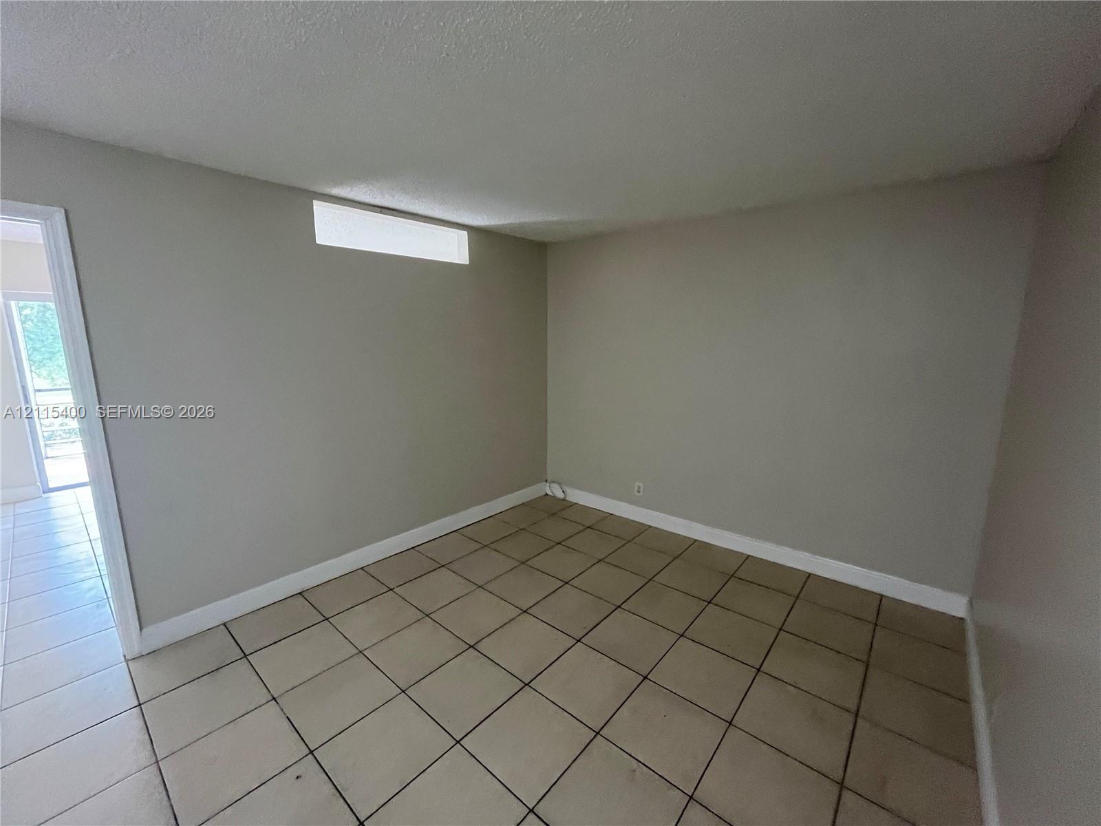 Neutral-toned interior space featuring ceramic tile flooring, a high-set horizontal window, and a door frame leading to a separate area