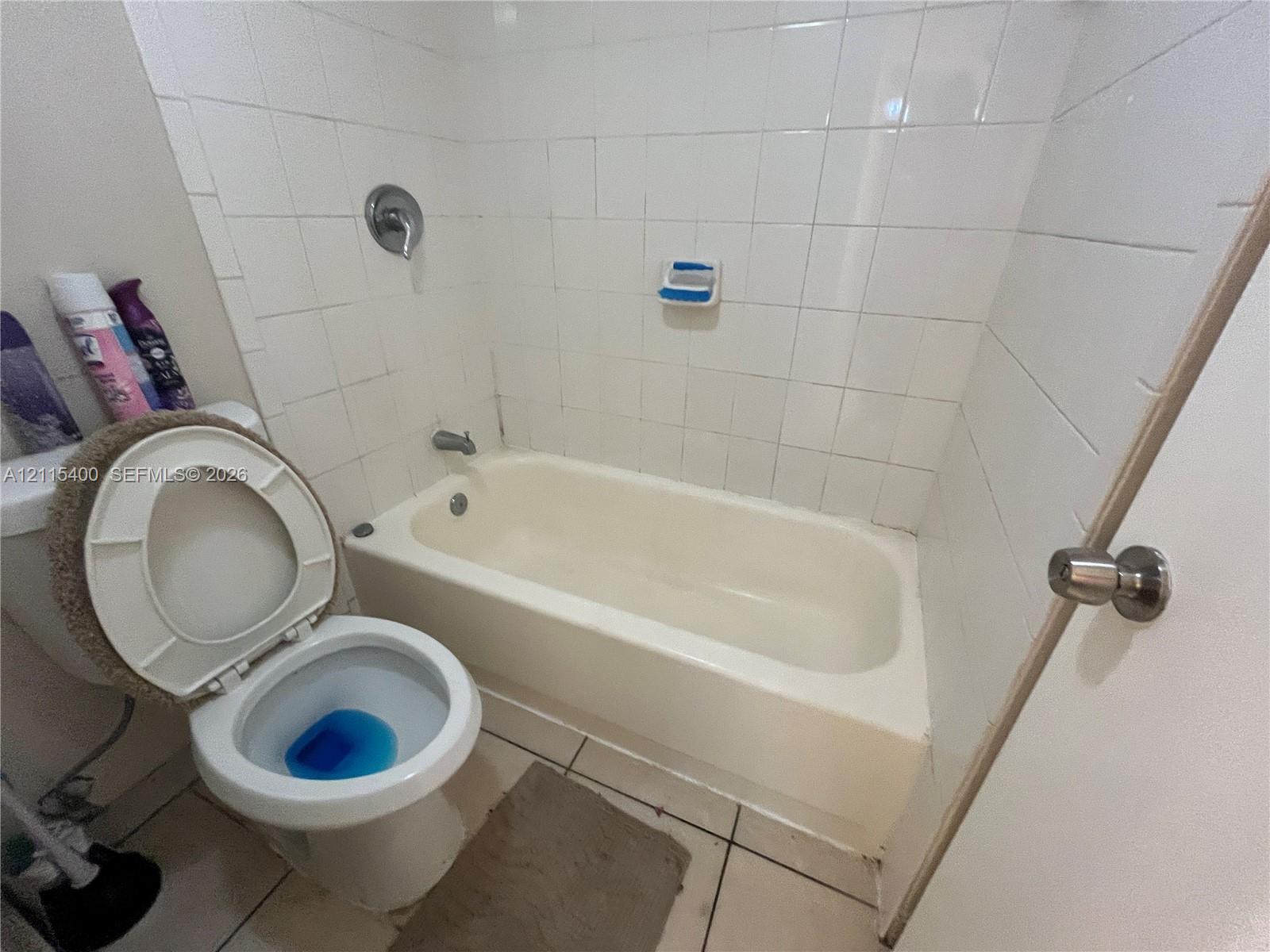 Bathroom featuring a porcelain tub with tile surround, chrome fixtures, and ceramic floor tile