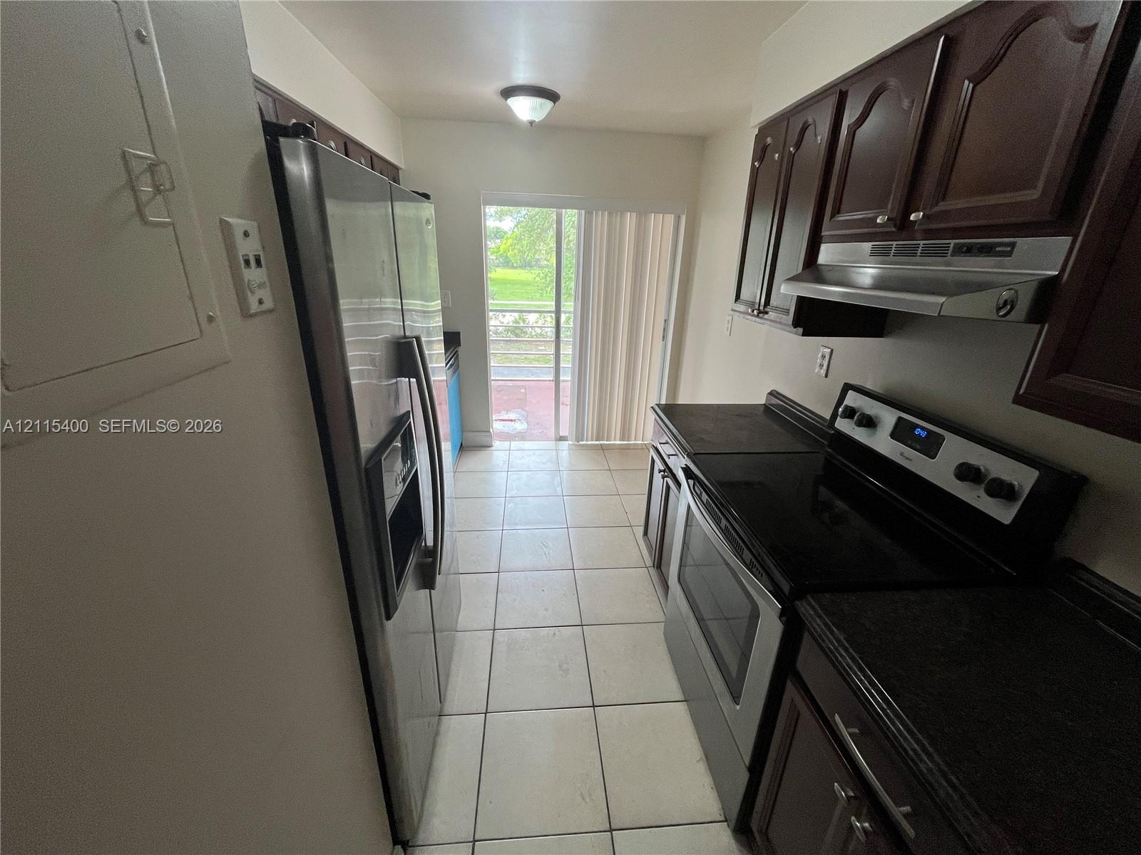 Kitchen featuring dark-finish cabinetry, stainless steel appliances, ceramic tile flooring, and sliding glass doors