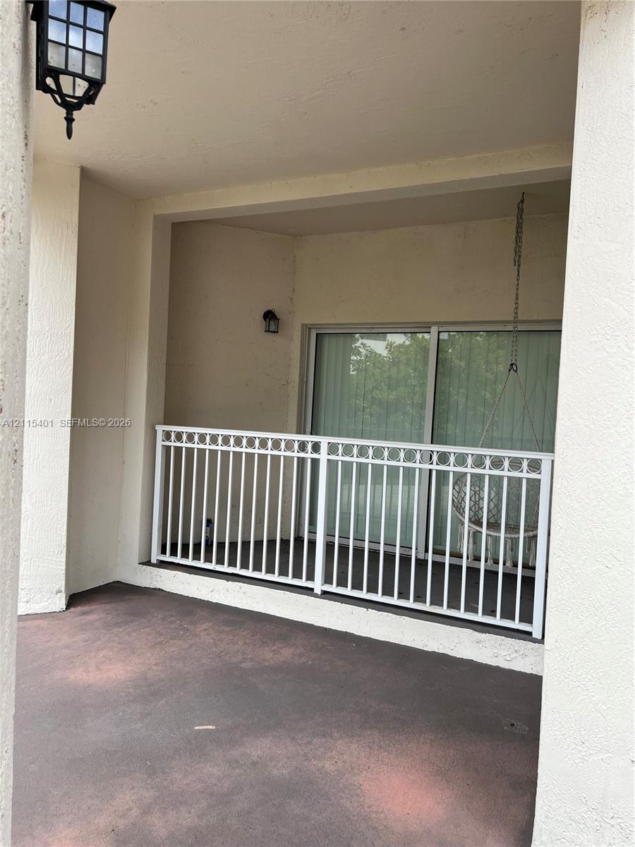 Covered balcony featuring concrete flooring, white metal railing with decorative top detailing, and exterior wall-mounted lantern lighting