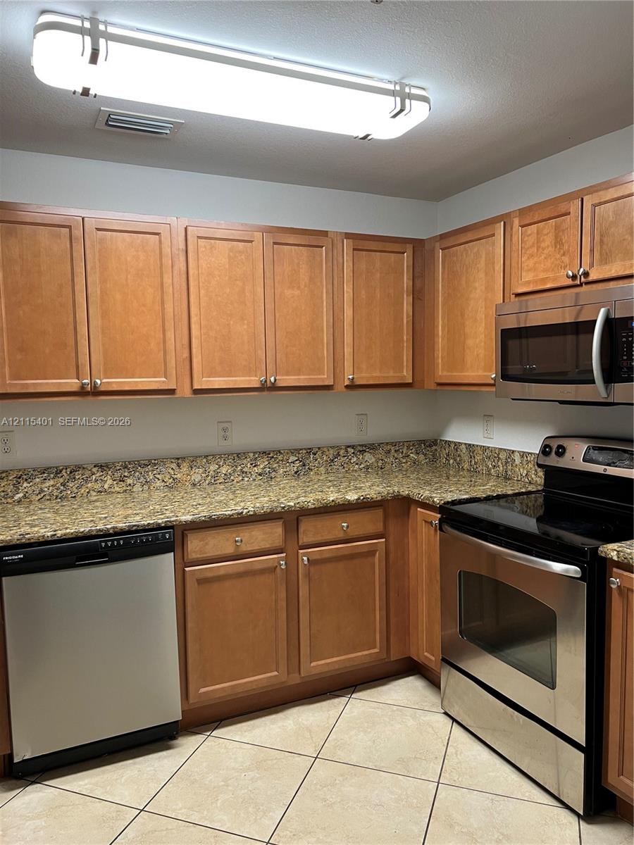 Kitchen featuring wood cabinetry, stone-surface countertops, stainless steel appliances, and tiled flooring