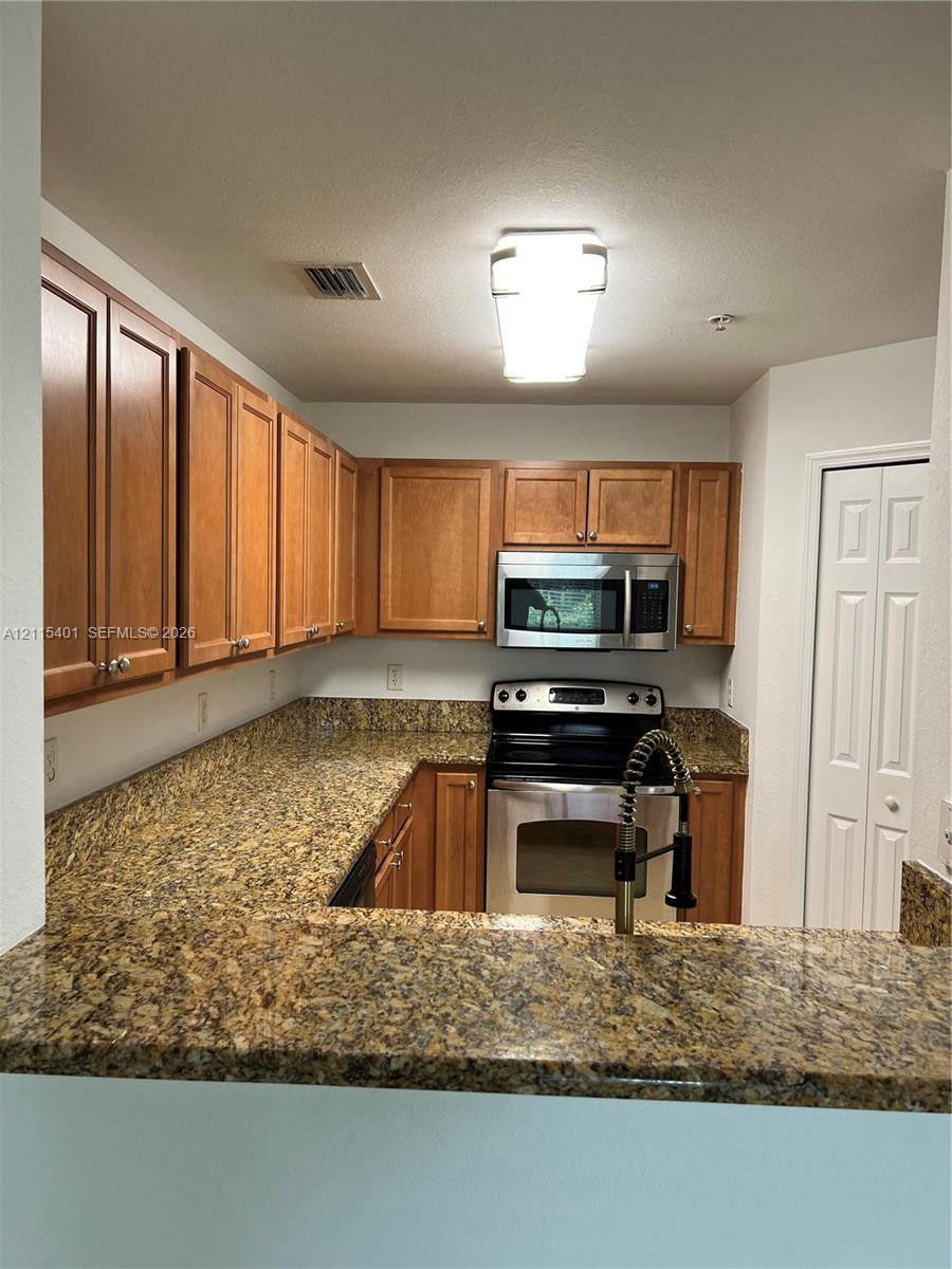 Kitchen featuring wood cabinetry, stone-surface countertops, stainless steel appliances, and a gooseneck faucet