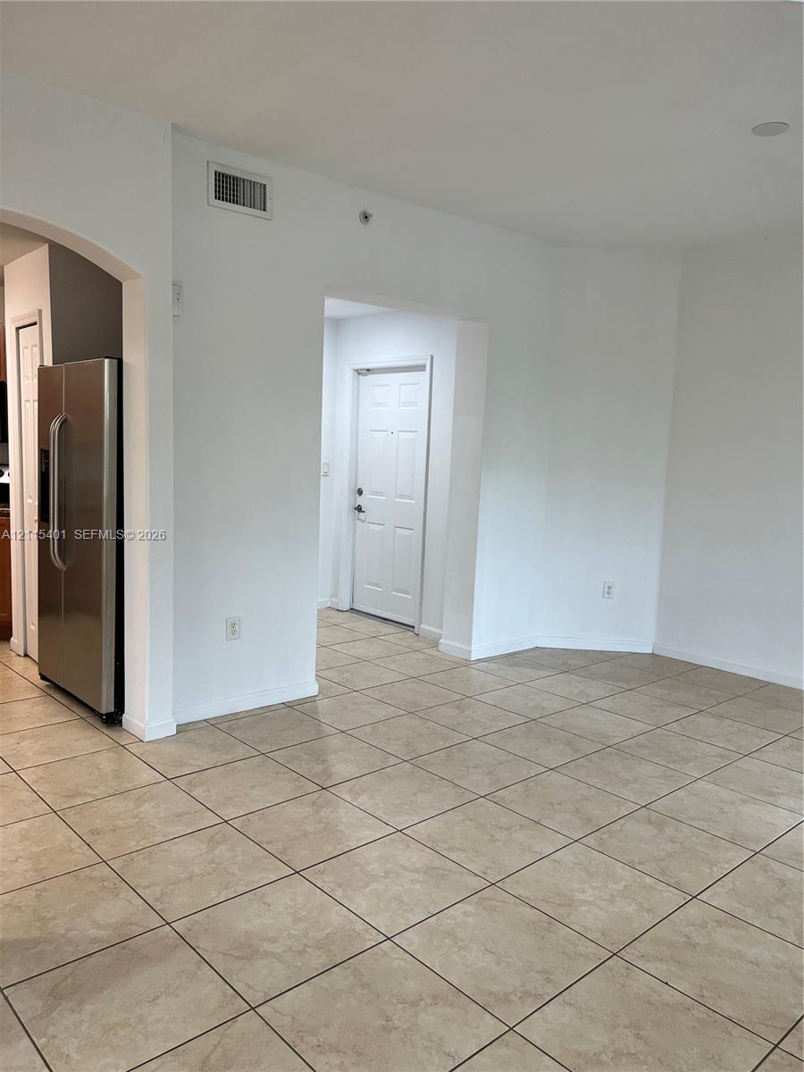 Neutral-toned tile flooring, arched entryways, and a stainless steel refrigerator