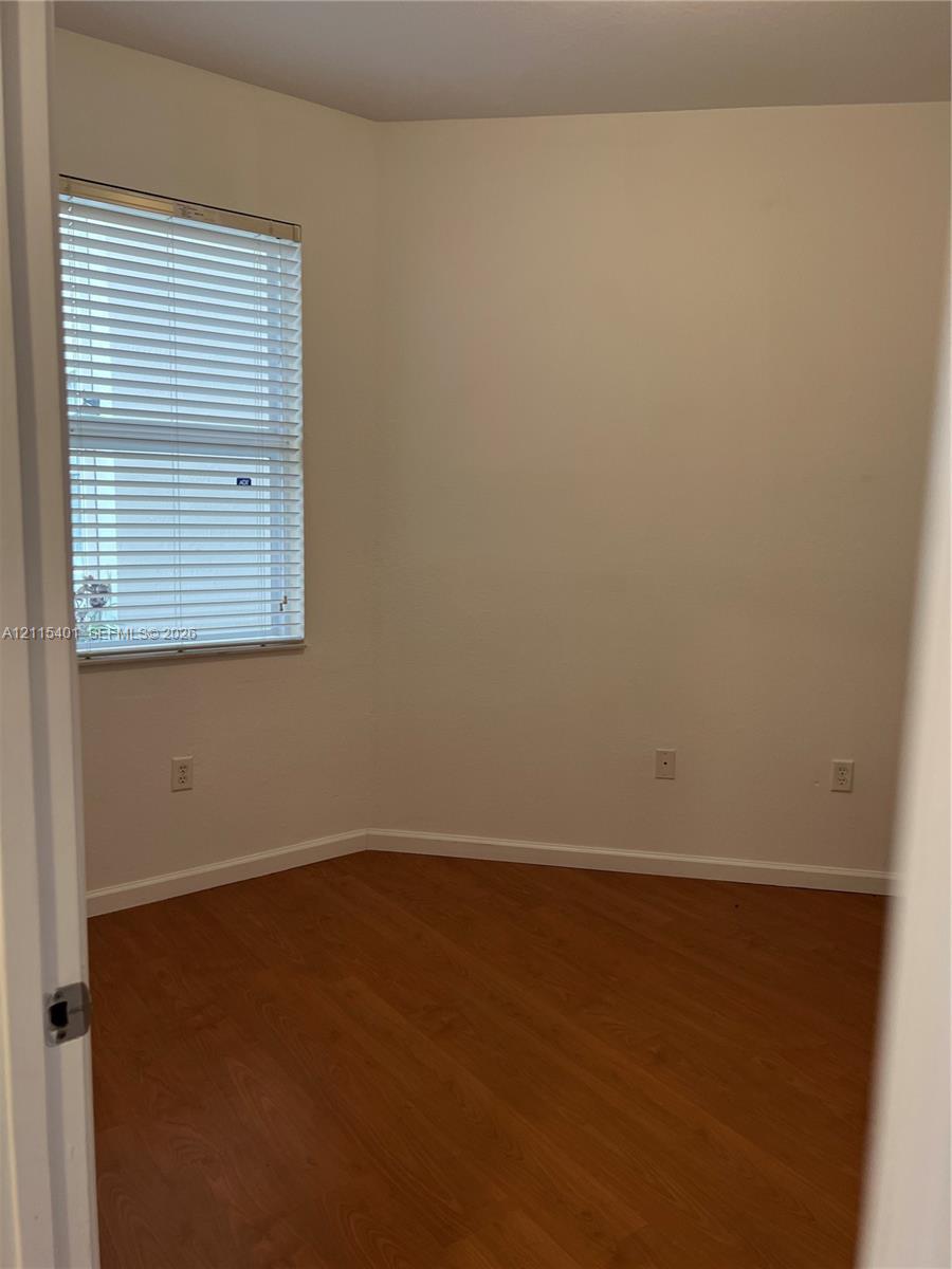 Neutral-toned room featuring wood-finish flooring and a window with horizontal blinds