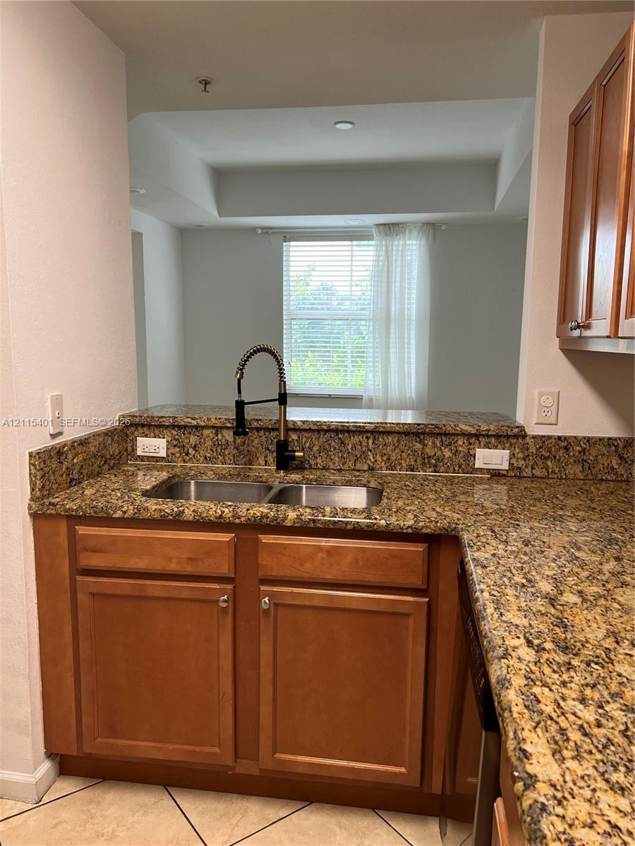 Kitchen featuring stone countertops, wood-finish cabinetry, a dual-basin stainless steel sink with a high-arch pull-down faucet, and tiled flooring