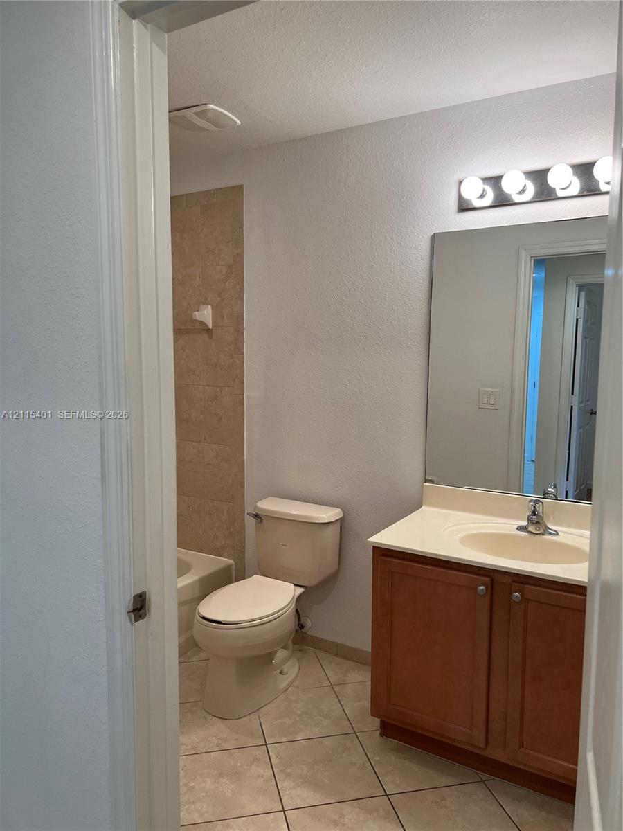 Bathroom featuring a wood-finish vanity with a molded countertop, a large wall-mounted mirror, ceramic tile flooring, and a tub enclosure with stone-style wall tile