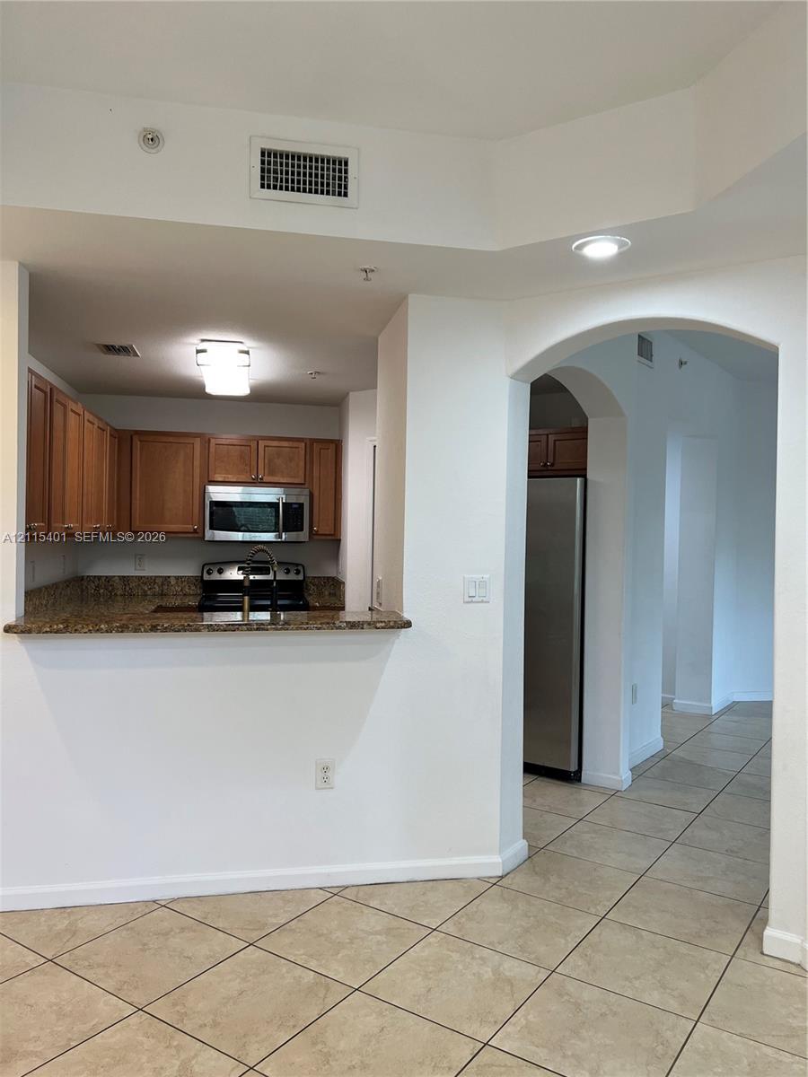 Kitchen featuring wood cabinetry, stone-surface countertops, stainless steel appliances, and tile flooring, highlighted by an arched architectural opening