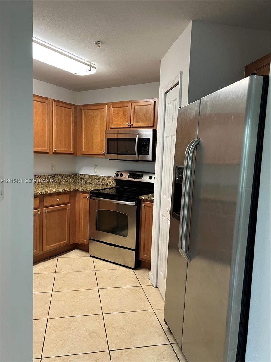 Kitchen featuring wood cabinetry, stone-finish countertops, stainless steel appliances, and tile flooring