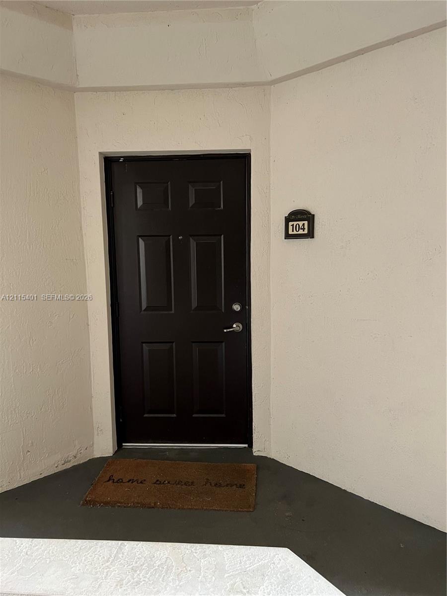 Dark-toned six-panel entry door featuring a metal lever handle and integrated deadbolt, set against a neutral-toned stucco exterior wall
