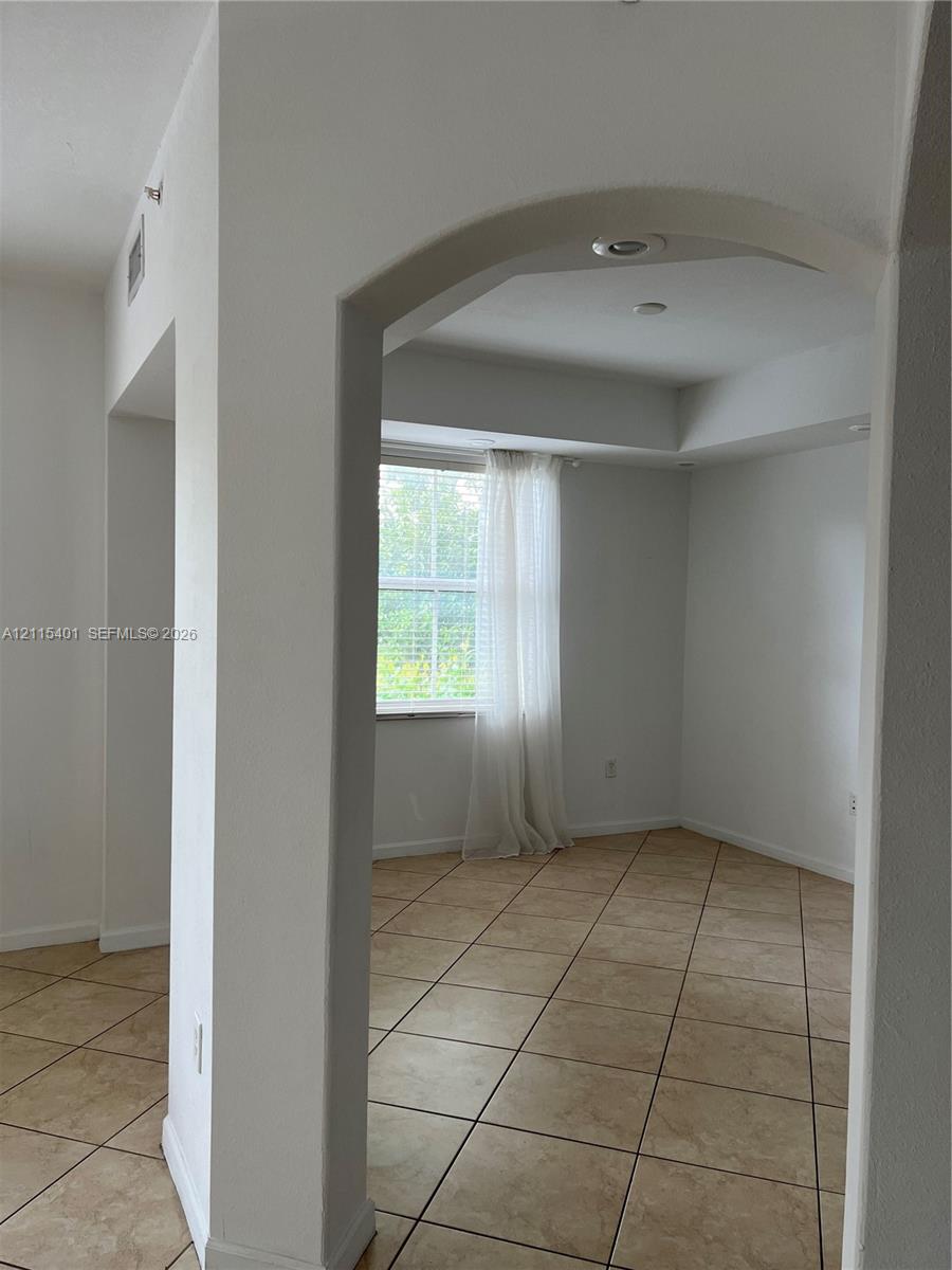 Arched entryway featuring neutral-toned tile flooring, recessed ceiling lighting, and a tray ceiling detail