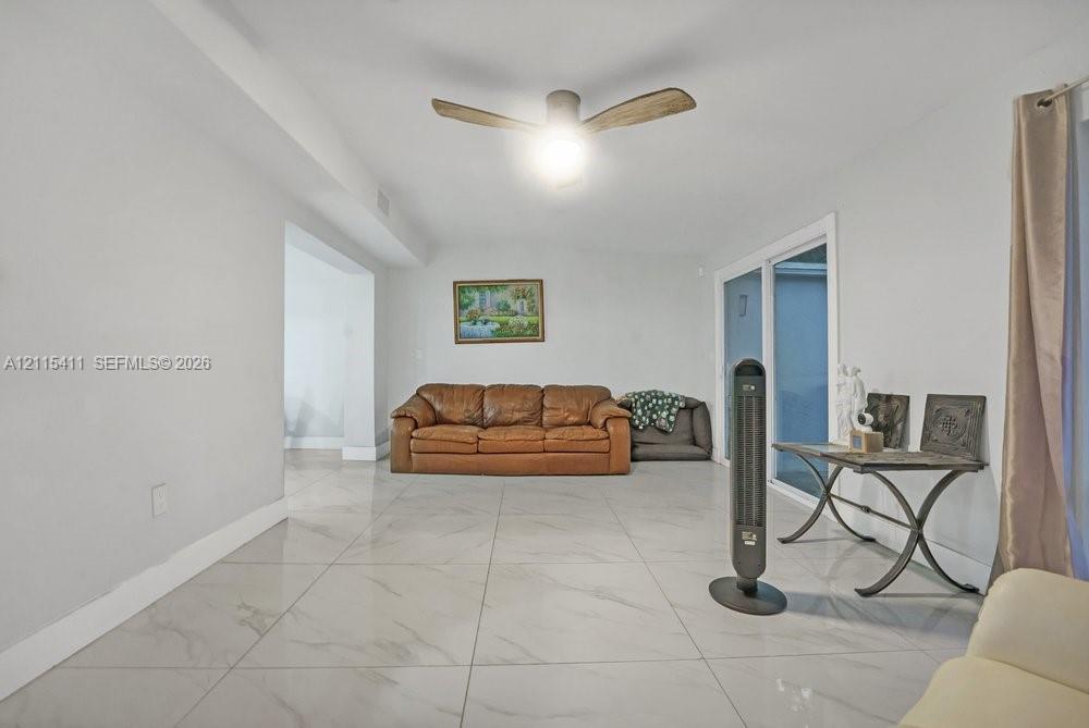 Large-format neutral flooring with stone-pattern detail, sliding glass doors, and a ceiling fan with integrated lighting