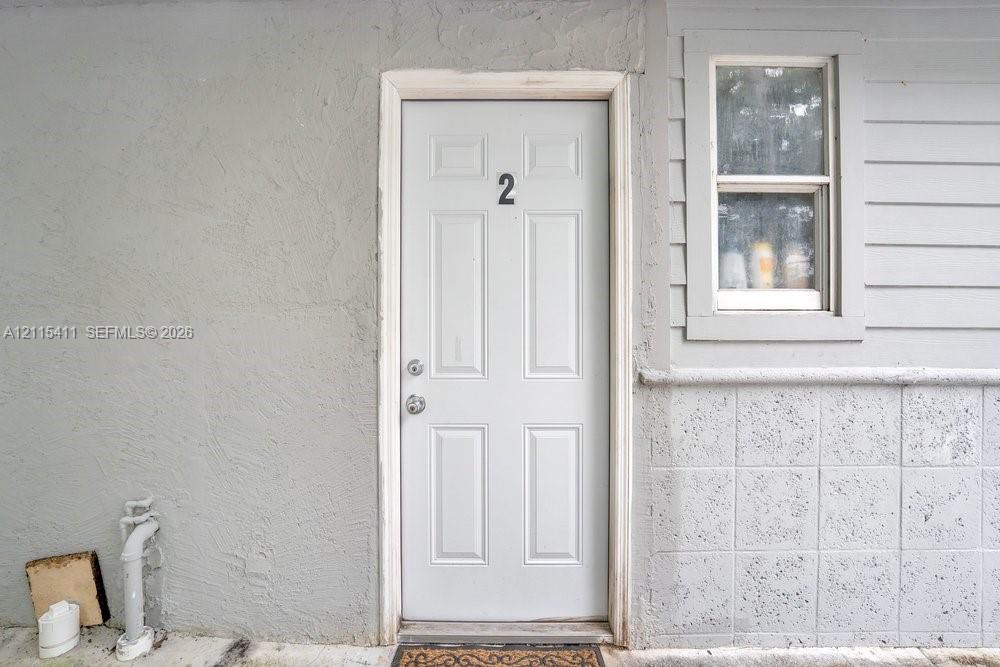 Exterior entry featuring a six-panel door, textured stucco wall finish, horizontal siding, and a square-pane window with masonry wainscoting