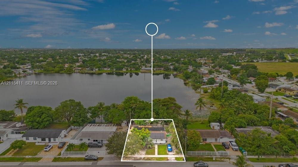 Aerial perspective of a single-story residence situated on a waterfront lot featuring direct lake frontage, mature trees, and a concrete driveway