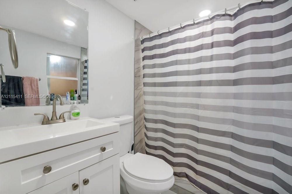 Bathroom featuring a white vanity cabinet with a rectangular basin, brushed-nickel faucet, large wall-mounted mirror, and tile shower surround