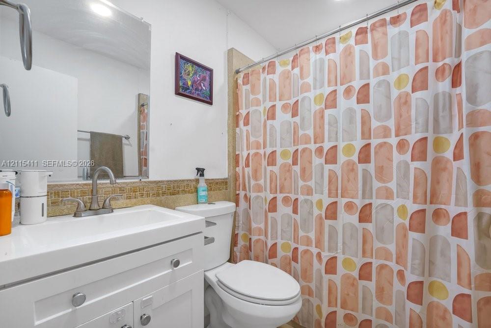 White vanity cabinet featuring a rectangular integrated sink, arched-neck faucet, mosaic tile backsplash, and a wall-mounted mirror