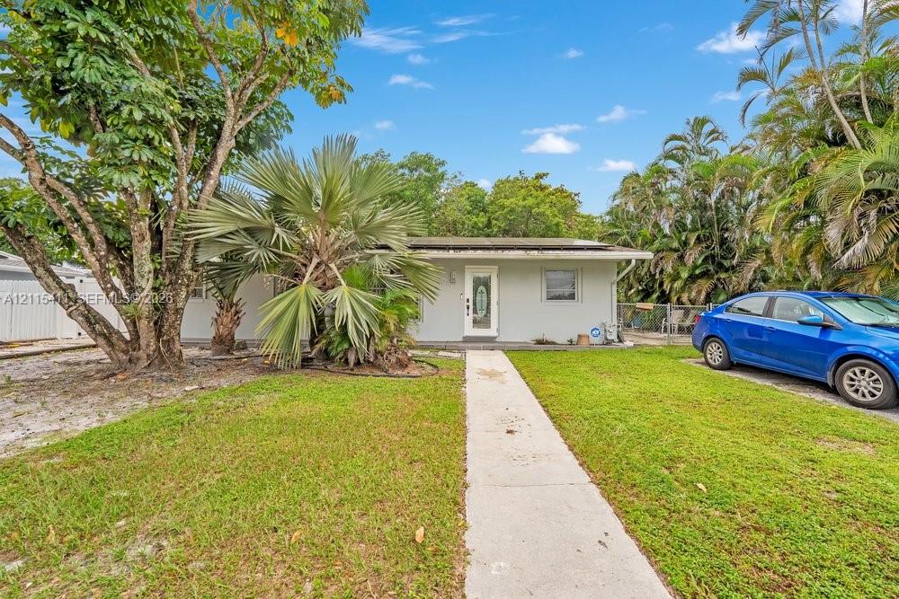 Single-story exterior featuring a light-toned stucco facade, a glass-panel entry door, and mature palm landscaping with a concrete walkway