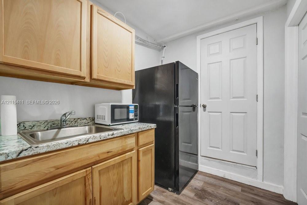 Light wood cabinetry with integrated storage, stone-finish countertops, stainless steel sink, and wood-finish flooring