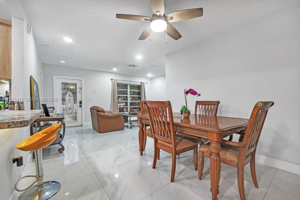 Large-format tile flooring, recessed lighting, ceiling fan with integrated light fixture, and exterior door with a decorative glass insert
