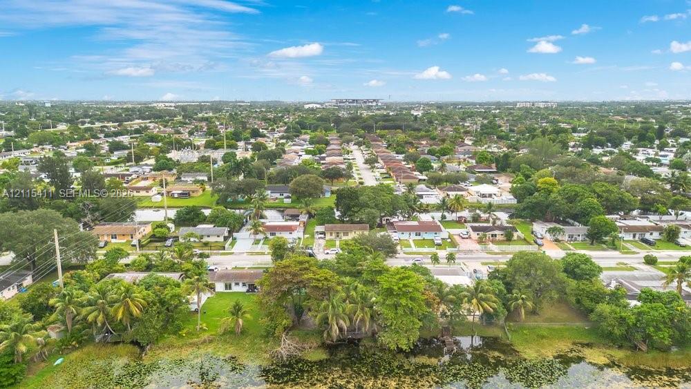 Aerial perspective featuring a waterfront lot, mature trees, and established residential neighborhood surroundings