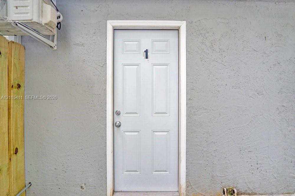Six-panel exterior door with metallic hardware, set within a light-toned stucco wall