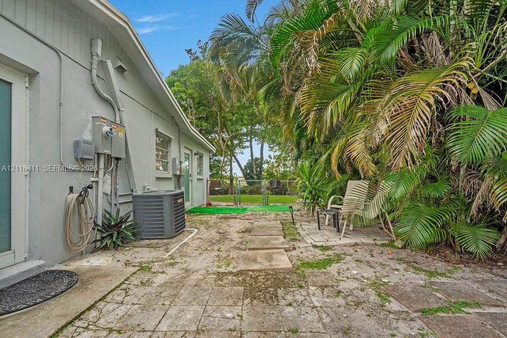 Exterior space featuring concrete paver hardscaping, mature palm trees, and perimeter fencing
