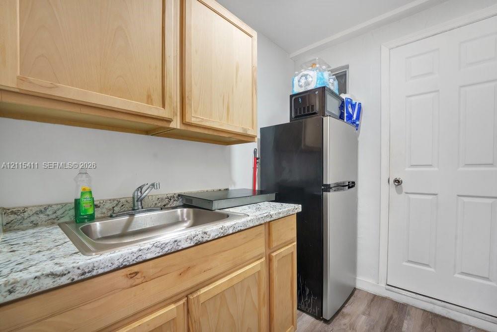 Natural wood-finish cabinetry, speckled stone-finish countertop, stainless steel undermount sink with gooseneck faucet, and six-panel interior door