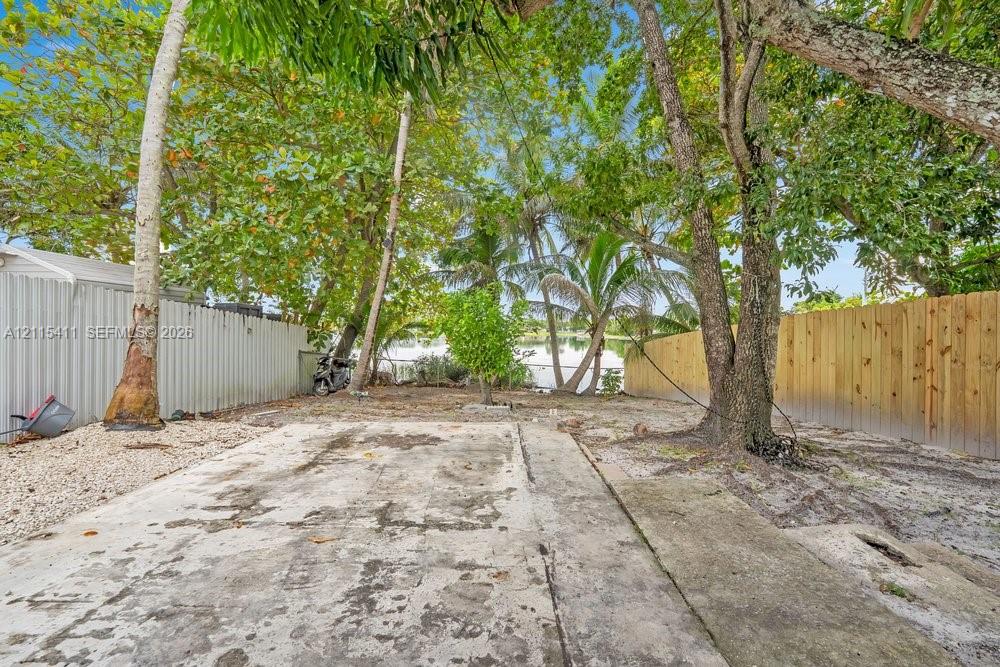 Outdoor area featuring a concrete slab, mature trees, wood-tone fencing, and corrugated metal privacy screening