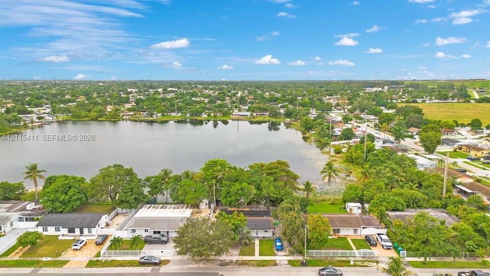 Aerial perspective featuring residential structures situated along a lakefront, incorporating paved driveways, fenced perimeters, and established mature trees