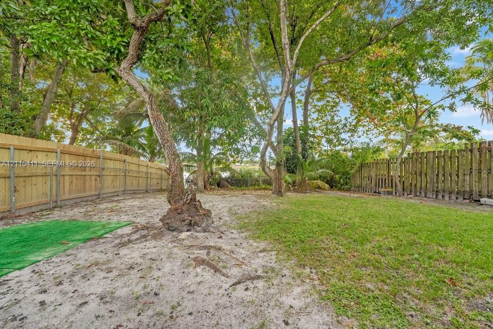 Backyard featuring a grass lawn, mature trees, and wood-panel fencing