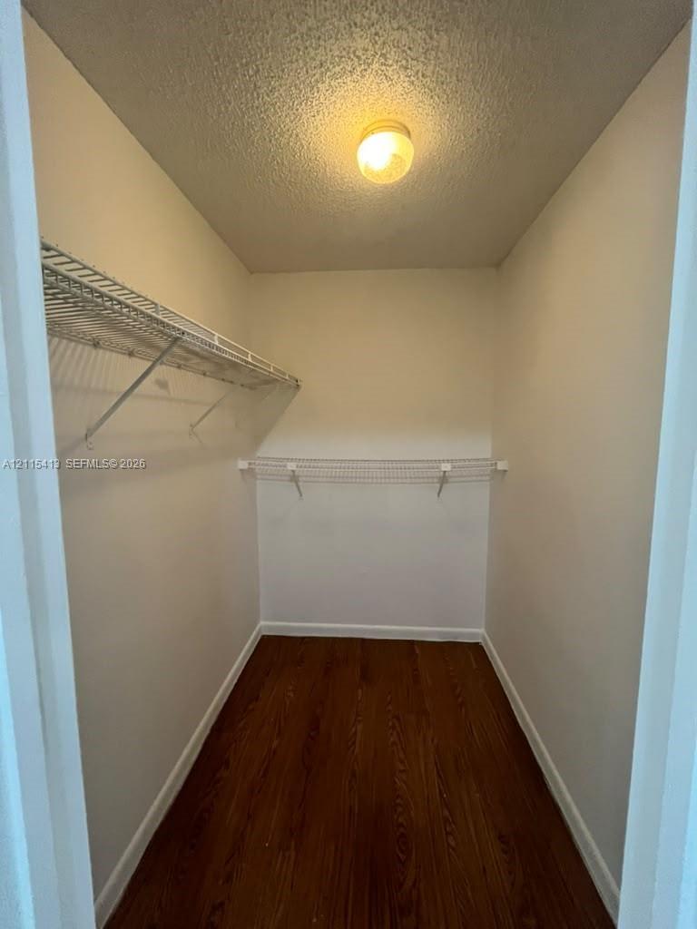 Storage space featuring wood-finish flooring, white walls, tiered wire shelving, and a central ceiling-mounted light fixture