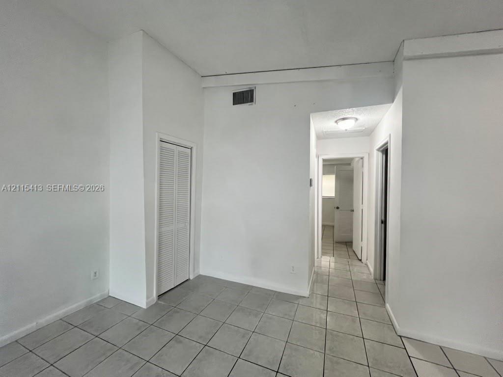 Neutral-toned ceramic tile flooring, high ceilings with exposed structural beam, and built-in louvered closet doors