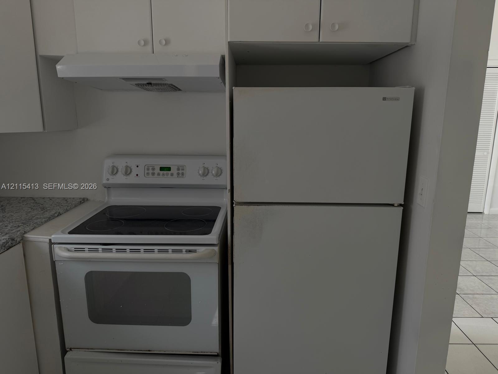 Kitchen featuring a white electric range, white top-mount refrigerator, white range hood, stone-finish countertop, and white cabinetry