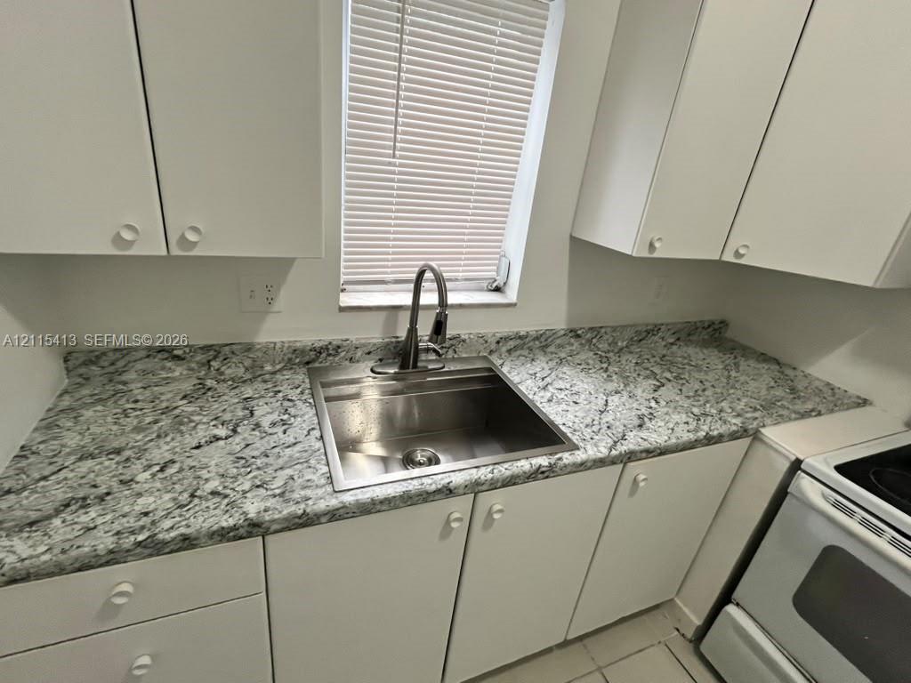 Kitchen featuring stone-patterned countertops, stainless steel undermount sink, high-arc pull-down faucet, white cabinetry, and window with blinds
