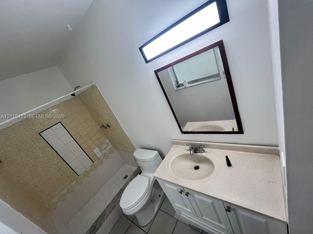 Bathroom featuring a vanity with a stone-finish countertop, undermount sink, tiled tub-shower surround, rectangular wall-mounted mirror, and linear light fixture