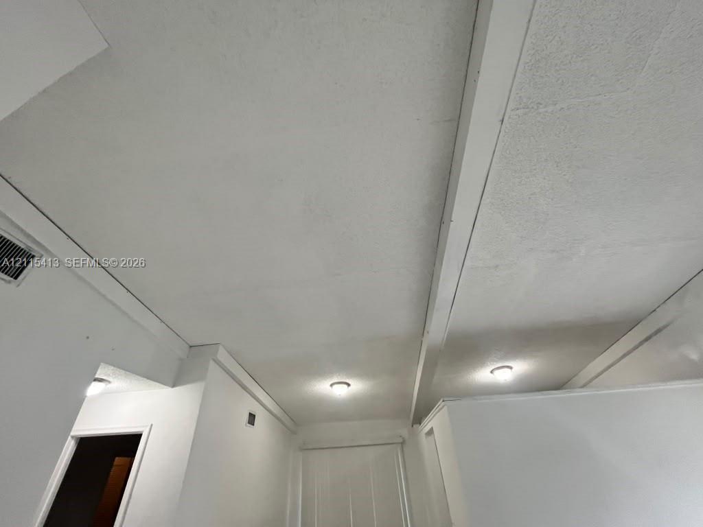 White textured ceiling featuring exposed structural beams and dual flush-mount light fixtures