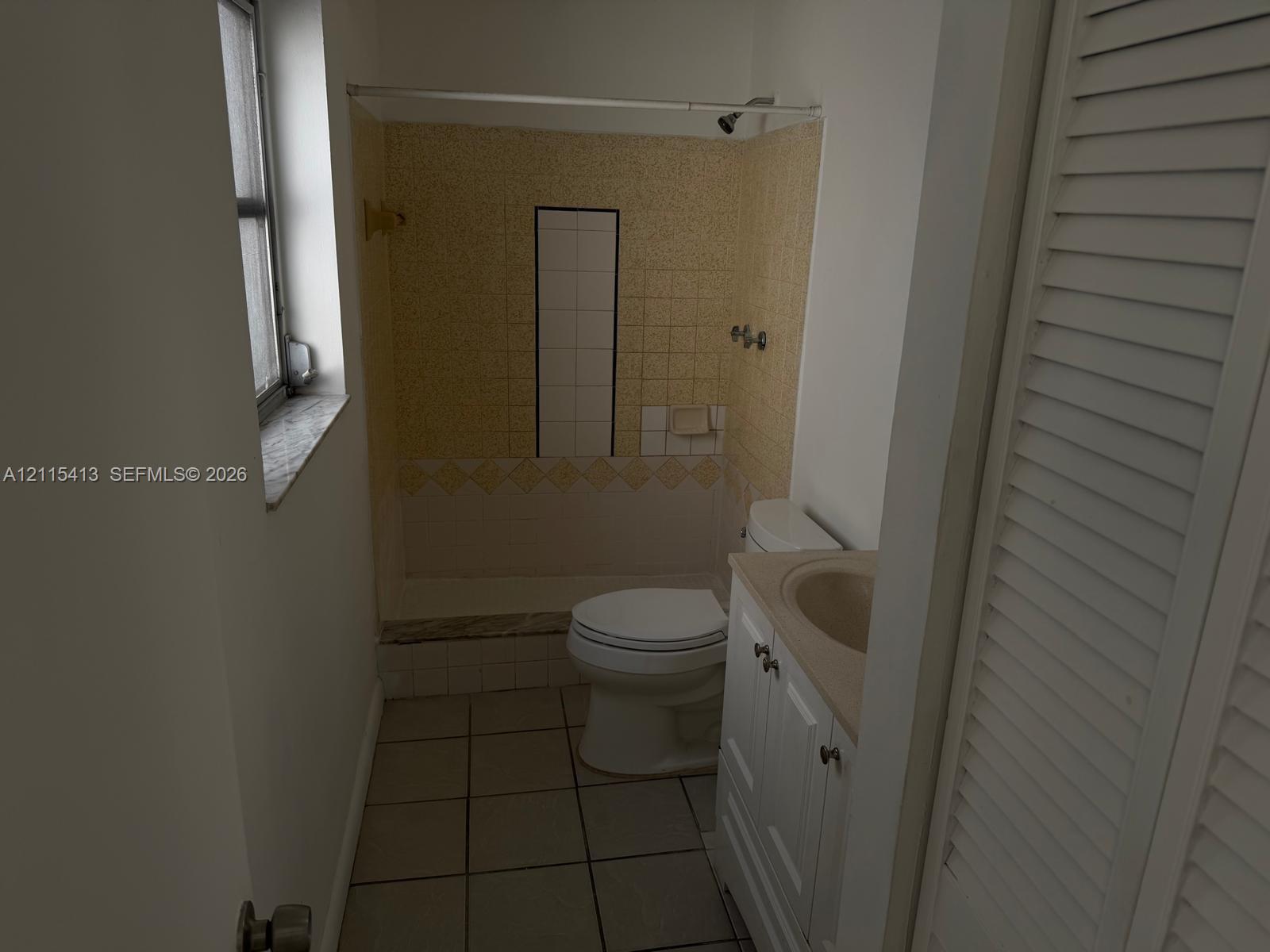 Bathroom featuring tiled floor, vanity with integrated sink, shower enclosure with tile surround, and louvered closet doors