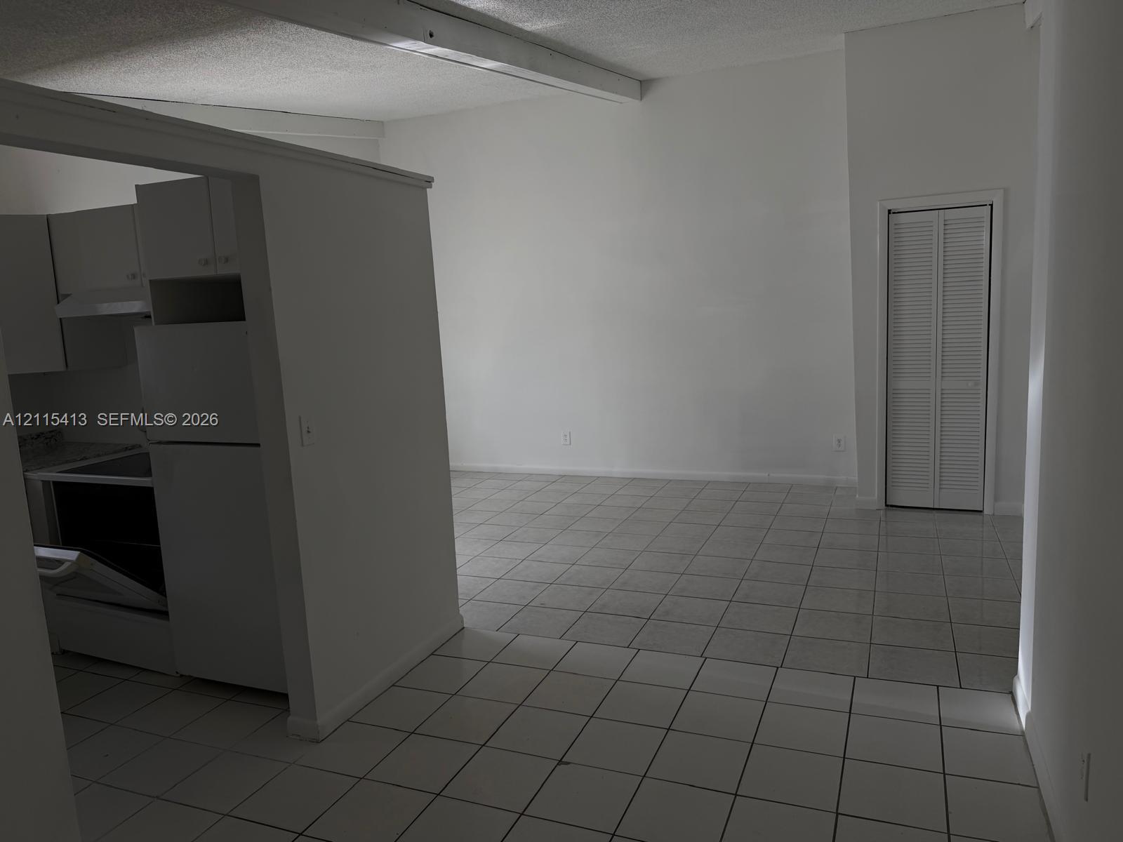 Interior featuring white ceramic tile flooring, neutral wall finishes, a built-in kitchen partition, and a white louvered closet door