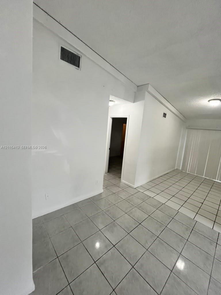 Interior space featuring light gray square tile flooring and white wall finishes, accented by ceiling-mounted lighting fixtures
